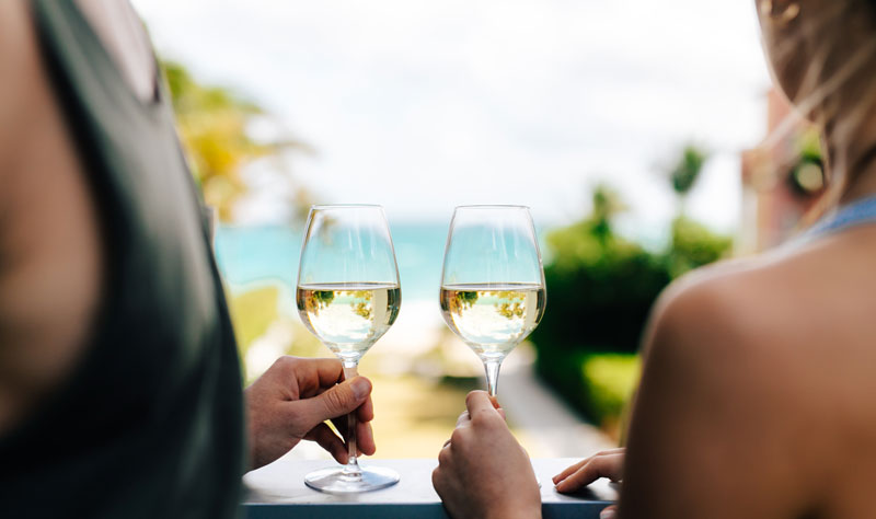 Man and woman holding wine glasses while overlooking the ocean.