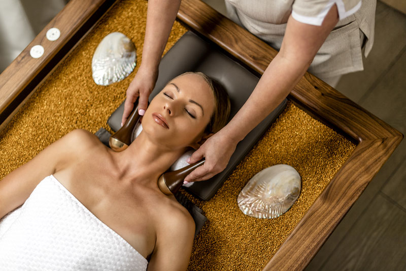 Woman laying on a massage bed filled with quartz, receiving a massage.