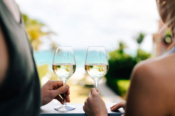 Man and a woman holding wine glasses with the ocean in soft focus in the background.