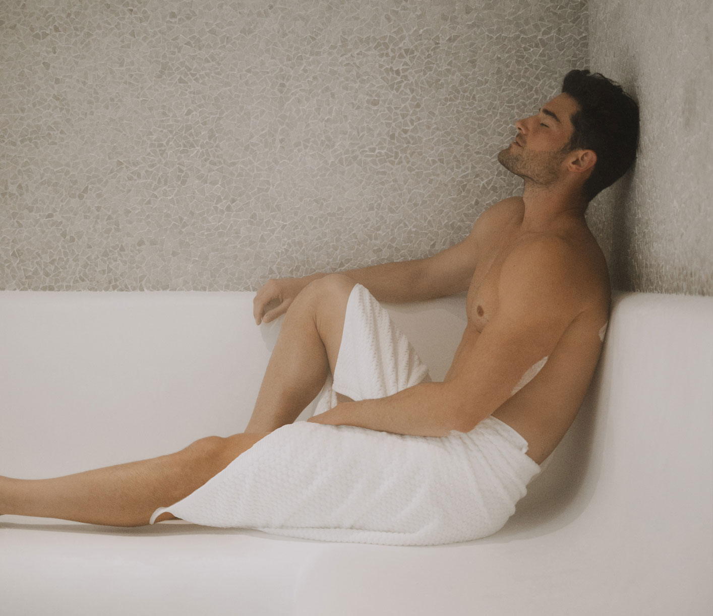 Man with eyes closed, reclined in a salt cave wrapped in a towel.