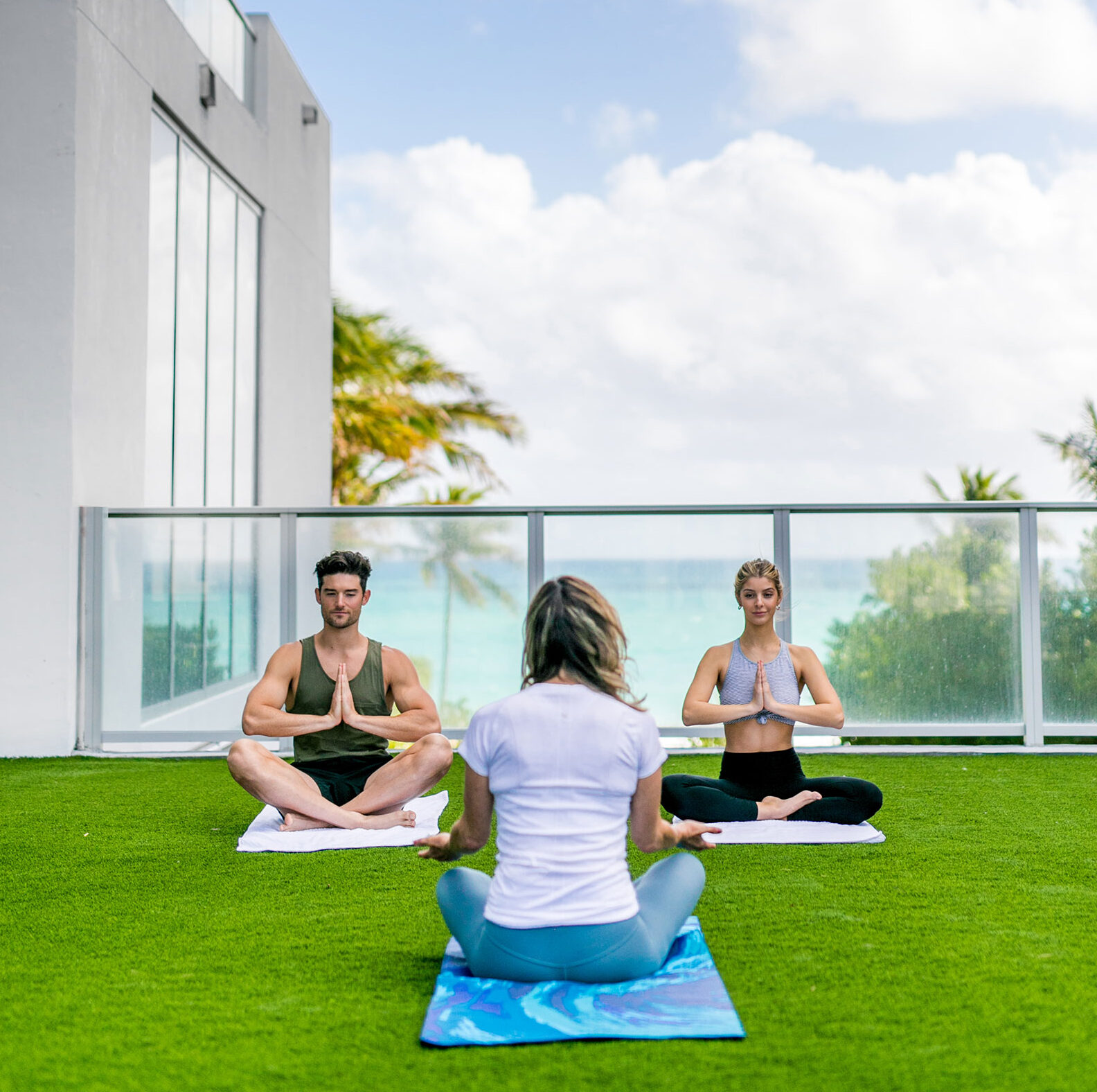 Three people sitting cross legged on a terrace overlooking the ocean doing yoga.
