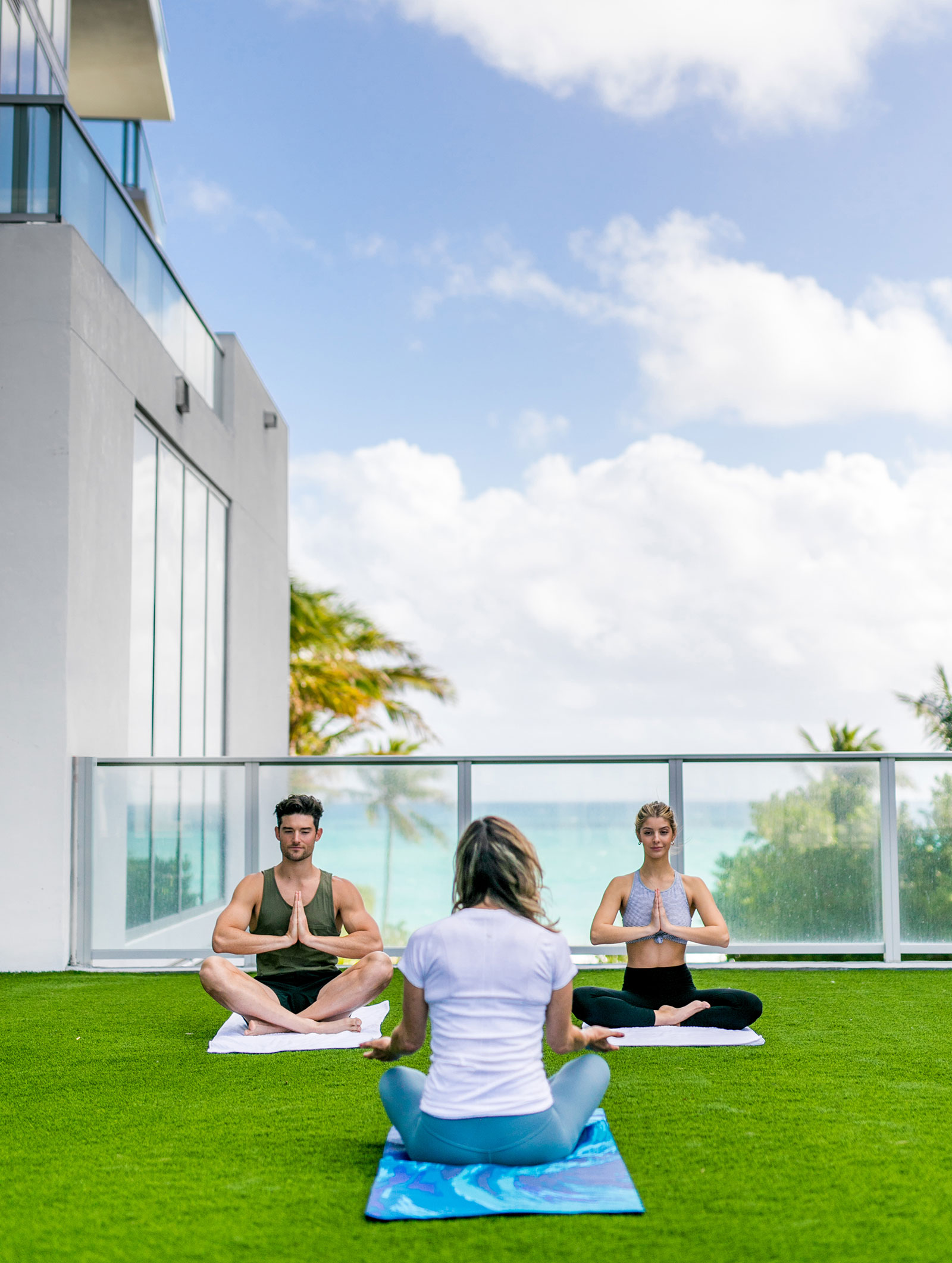 Three people sitting cross legged on a terrace overlooking the ocean doing yoga.