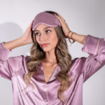 Woman wearing pink silk pajamas with eye mask on top of her head. 