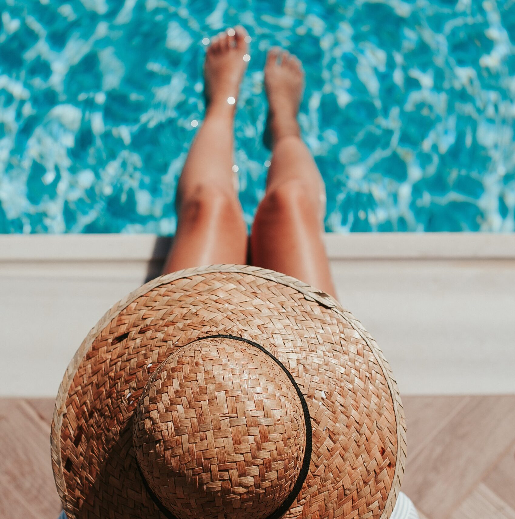 Woman wearing a straw hat sitting at the edge of a pool.