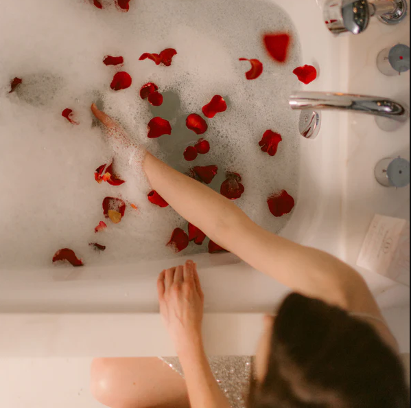 woman reaching into a bubble bath with rose petals